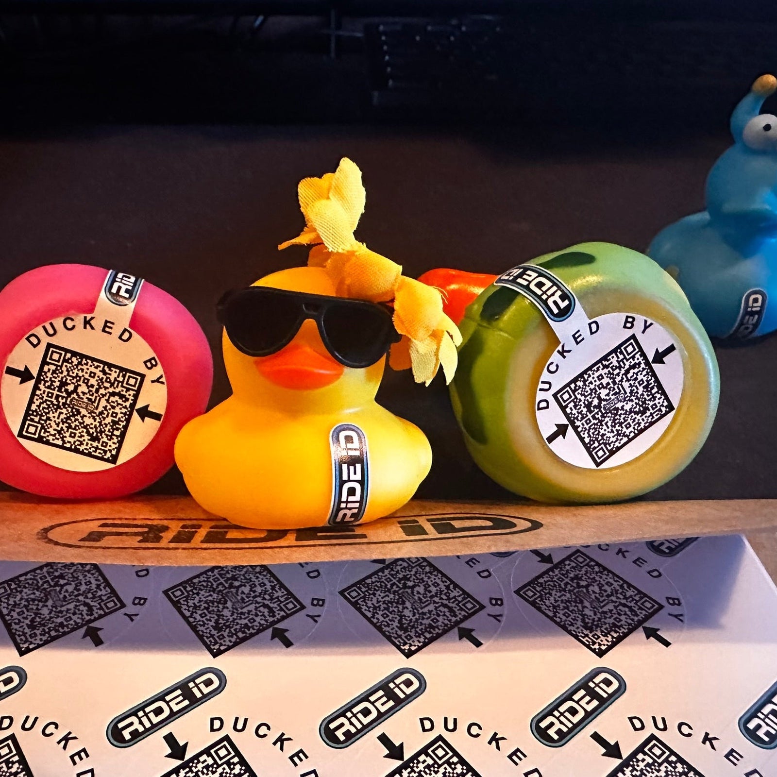 Rubber ducks wearing Ride ID DUCKED BY QR code Duck Tags beside a sheet of tags